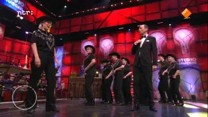 Foto van de studio van Snugger waarbij op het podium de presentator staat met aantal andere mensen.