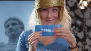 Foto van vrouw, portret, met plastic helm op die papiertje vasthoudt met "geheim" erop.