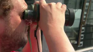 Foto, close-up, van het gezicht van een man die door een verrekijker kijkt.