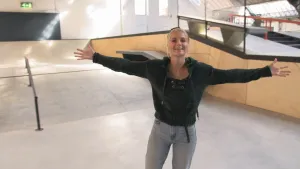 Foto van presentator die met haar armen wijd staat in een ruimte in een gebouw, een skatepark.
