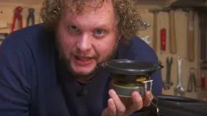 Foto van presentator, je ziet met name zijn hoofd, die een rond luidsprekertje vasthoudt.