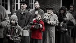 Oude foto, zwart/wit, met mensen en kinderen die in de rij staan ten tijde van de Tweede Wereldoorlog, één meisje in die rij is haar jas ingekleurd, rood.