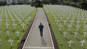 Foto van een soldatenkerkhof, met vele witte kruizen die staan in grasveld, van bovenaf gezien waarop een man loopt overt een pad erdoorheen.