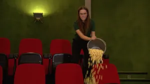 Foto van vrouw die in een bioscoopzaal een emmer met popcorn leeggiet voor rij bioscoopstoeltjes.