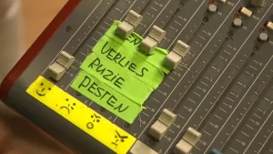 Foto van een knoppenpaneel met stukjes tape erop geplakt met woorden erop (verlies, ruzie, pesten) en een reeks sombere emoticons.