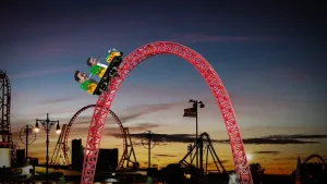 Foto van een achtbaan in de schemering met en karretje met twee personen erin die over een hoge steile heuvel rijdt.