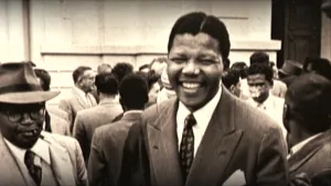 Oude foto van zwarte man, Nelson Mandela, met meerdere mensen achter hem, zwart/wit.