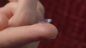 Foto, close-up, van een duim waarop een contactlens ligt.