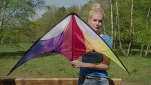 Foto van presentator die buiten in de natuur een kleurrijke symmetrische vlieger vasthoudt.