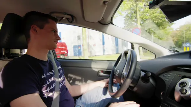 Foto van een man die met zijn handen op schoot achter het stuur van een auto zit.
