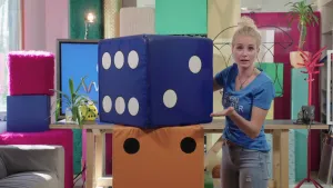 Foto van presentator bij een heel groot nagemaakte blauwe dobbelsteen in de studio.