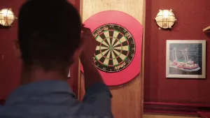 Foto van iemand van achteren gezien die een pijltje naar een dartbord werpt.