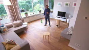 Foto van presentator in een moderne huiskamer met aantal objecten op de grond waaromheen witte cirkels staan getekend.