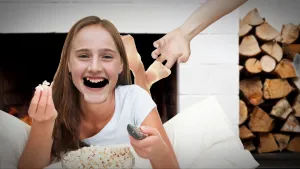 Foto van een vrolijk lachend meisje dat op haar buik op bed ligt die door iemand op haar blote voet wordt gekieteld.