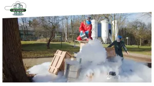 Foto van een proefopstelling buiten in tuin waarbij iemand vloeibare stikstof uit een bak giet en je ziet net witte rook die ervan af komt.