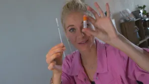 Foto van presentator die een wattenstaafje en een klein buisje met dopje, soort flesje, vasthoudt.