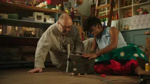 Foto met man en nog een persoon op de grond van een kamer met veel spullen die zitten bij een filmprojector.