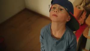 Foto van een jongetje met bril en een pet op in kamer.
