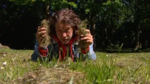 Foto van presentator die op het gas ligt en houdt droog gras/hooi vast, in beide handen wat.