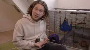 Foto van presentator bij een dierenhok binnen en houdt een klein dier vast in zijn handen.