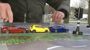 Foto van drie speelgoedautootjes op een namaak weg, die autootjes wachten voor een namaak stoplichtje.