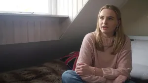 Foto van een meisje dat zit op een bed in slaapkamer die iets vertelt.