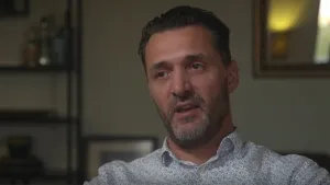 Foto van een man, portret, die iets vertelt, in een huiskamer.