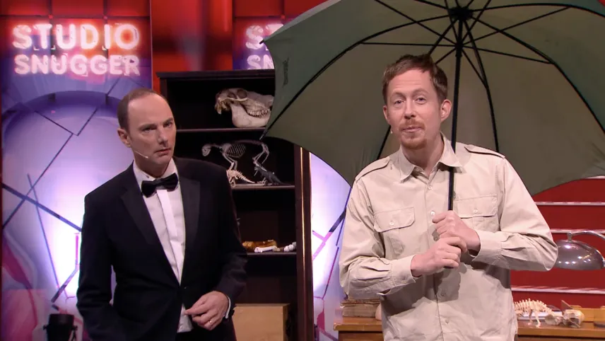 Foto van Studio Snugger met twee mannen op het podium, één van hen houdt een paraplu vast, verder staat er een kast.