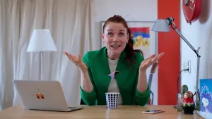 Foto van presentator achter laptop aan tafel/bureau in woonkamer.