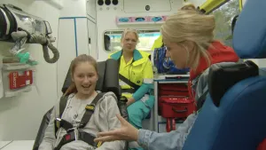 Foto van een meisje op brancard in een ziekenauto, haar moeder en een verpleegster zitten bij haar.