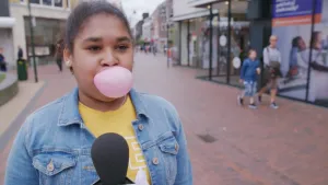 Foto van een meisje in winkelstraat die een roze kauwgum bel blaast.