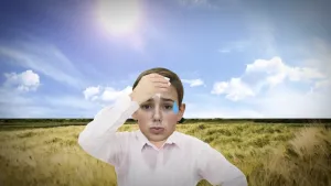 Foto van zwetend jongetje met op de achtergrond grasvlakte en felle zon, blauwe hemel.