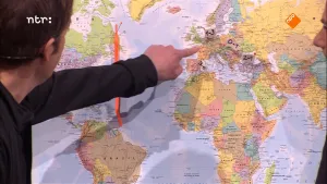 Foto van man, je ziet vooral zijn arm en hand, die Europa op een grote wereldkaart aanwijst.