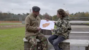 Foto van twee mannen op stenen muurtje buiten en laten eenvoudige kaart van een land zien.