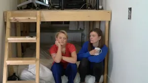 Foto van twee vrouwen met bezorgde gezichten die op de onderste verdieping van een stapelbed zitten.