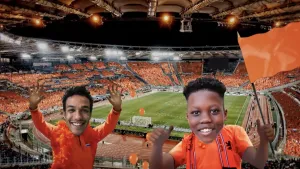 Foto van twee jongetjes in Oranje outfit met op de achtergrond voetbalstadion met voetbalveld en veel toeschouwers in het oranje.