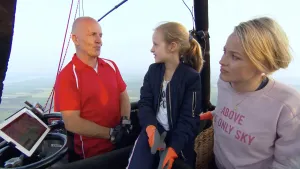 Foto van vrouw en jong meisje en de piloot in de gondel/mand van een heteluchtballon, je ziet ook wat van het uitzicht.