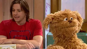 Foto van scène uit Sesamstraat met presentator en Tommie (pop) aan de desk.