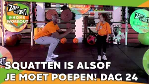 Foto van scène uit Zapp Sport met Steven Brunswijk en zijn dochter op het podium, het logo in beeld, sportartikelen op de achtergrond, erbij de tekst "squatten is alsof je moet poepen! dag 24".