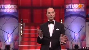 Foto van presentator in Studio Snugger, in de studio, met trap op de achtergrond en het logo.