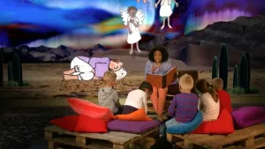 Foto van iemand die voorleest aan kinderen met op de achtergrond een decor uit een bijbelverhaal.