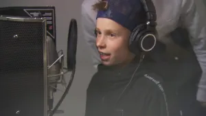 Foto van jongetje met oortelefoon op voor een microfoon en geluidsapparatuur in de geluidsstudio.