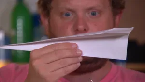 Foto van het hoofd van presentator die een papieren vliegtuigje vasthoudt.