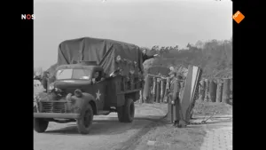Foto van het NOS-Journaal met zwart/wit foto waarop een legervoertuig, soort vrachtauto, staat met wat mensen erbij.