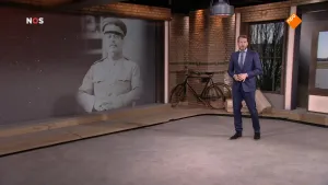 Foto van het NOS-Journaal met nieuwslezer die staat in ruimte met een grote zwart/wit foto van een generaal.