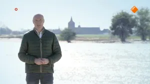 Foto van het NOS-Journaal met presentator voor een heel grote kleurenfoto van een rivier met kerk op de achtergrond.
