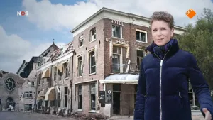 Foto van het NOS-Journaal met vrouw die staat voor een heel grote kleurenfoto van een straat in een stad, met Hotel De Wereld.