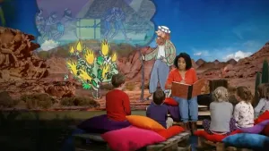 Foto van iemand die voorleest aan kinderen met op de achtergrond een decor uit een bijbelverhaal.