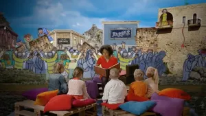 Foto van iemand die voorleest aan kinderen met op de achtergrond een decor uit een bijbelverhaal.