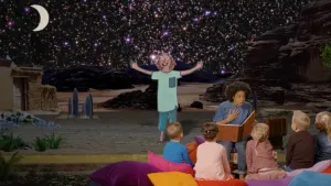 Foto van presentator die aan kinderen voorleest, zitten op toneel met op achtergrond tekening van een blijde jongen met sterren en maan achter hem.